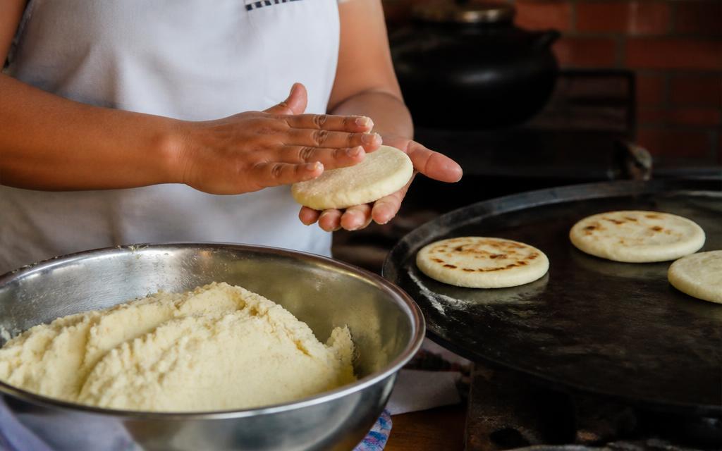 Manos formando arepas de masa de maíz junto a un budare caliente